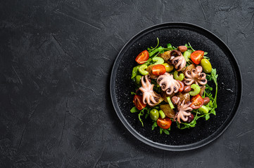 Salad with grilled octopus, potatoes, arugula, tomatoes and olives. Black background. Top view. Space for text