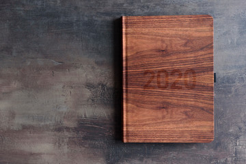 Top view of personal calendar lay on a table. Wooden pattern cover with 2020 year. Marble table with copy space. New year planning concept.