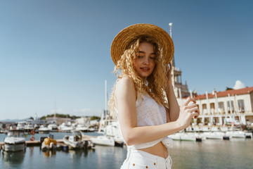 Fototapeta premium curly blonde in a hat on the background of the seaport and boats