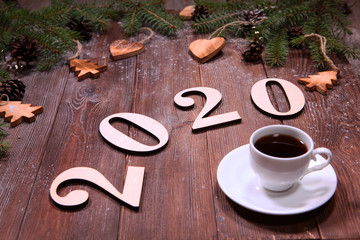 Figures 2020 and a Cup of coffee on a wooden background with Christmas toys. The concept of New year or Christmas. Copy space. Background for designers.