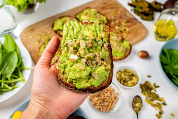 Avocado Guacamole Sandwich in a female hand with pumpkin seeds and wheat seedlings