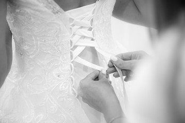 Mother or bridesmaids laces up wedding dress corset. Black and white photo