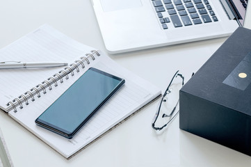 Closeup view of smartphone on open notebook on white table.