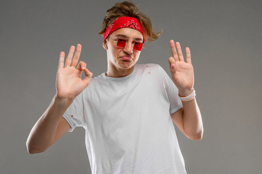 stylish blond guy with a bandana in glasses and a white T-shirt shows okay on a gray background