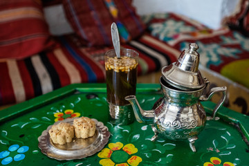 Closeup view of traditional sweet tasty Tunisian tea with pine nuts and cookies served on table. Horizontal color photography.