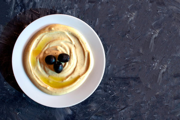 Famous traditional Arabic cuisine - dip Tahini with olives on dark gray background with copy space. Flat lay, top view. Tahina sauce.  