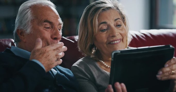 Close up of happy mature senior couple is making a selfie or video call with a tablet in living room at home.