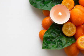 landscape of kumquats (tangerines) laid out on a white background with a lit candle. Relaxing backdrop for spa treatments.With drops of dew.