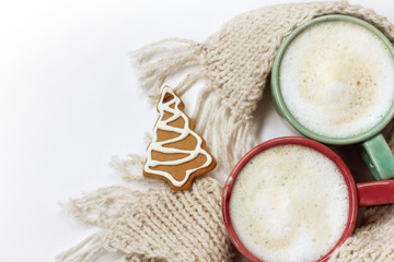 red and green cups with foamy coffee wrapped in a knitted scarf and decorated with ginger Christmas tree top view. winter festive coffee for two