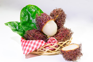 Rambutan (lychee) on a white background with space for text. In a small basket with green leaves.