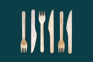 Set of disposable wooden knives and forks on a dark green emerald background. The concept of plastic fre, zero waste, environmental protection. Minimal simple creative layout in trendy color