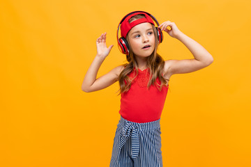 portrait of a cute charming young girl in a casual look with red headphones on a yellow background
