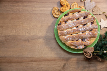 Pie with filling on a wooden background, next to toys and Christmas tree branches. The view from the top. The theme of Christmas and New year. Toned.