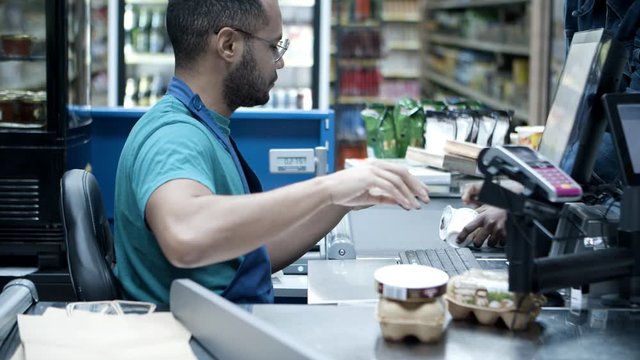 Serious African American Cashier Scanning Goods At Checkout. Focused Young Man In Eyeglasses At Workplace. Shopping Concept