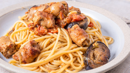 Spaghetti with homemade sausages and eggplant in a plate close-up - traditional Italian rural lunch