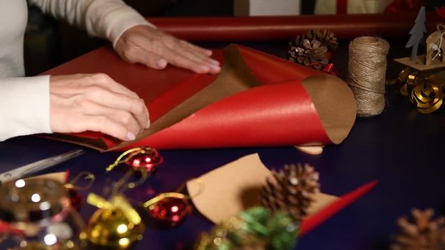 Close up on a women wrapping gifts for Christmas in red craft paper. The gift is decorated with strings and wood decorations. Edible Christmas gift for a zero waste Christmas.