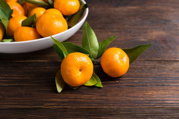 Tangerines mandarin with leaves in a plate on wooden background. Symbol Christmas food, copy space.