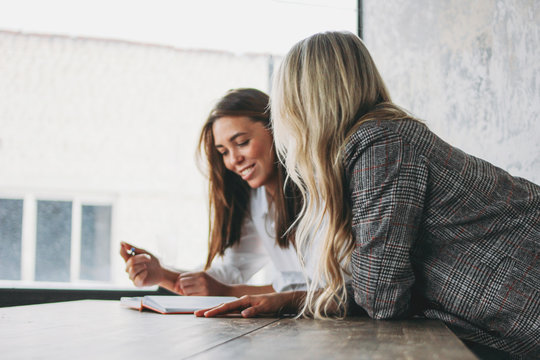 Young successful women colleagues discuss joint project, coaching or mentoring in modern loft office