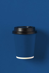 Cardboard blue coffee cup on classic blue background top view