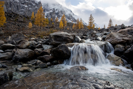 Small waterfall from stream high in mountains. Against background of snowy peaks. Beautiful photo
