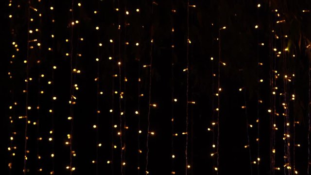 Many glowing golden lights of led holiday garlands shining in darkness of night. Abstract festive background. Real time 4k video footage.