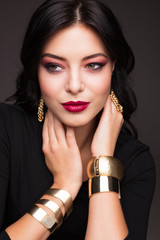 Portrait of beautiful young woman with  perfect bright makeup. Glamorous girl with gold bracelets and earrings. High resolution image.