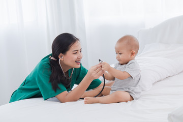 Asian toddler girl get sick examine by pediatrician doctor woman green uniform hold stethoscope, mother or nurse monitoring heart pulse rate adorable infant on bed in clinic, baby health care concept