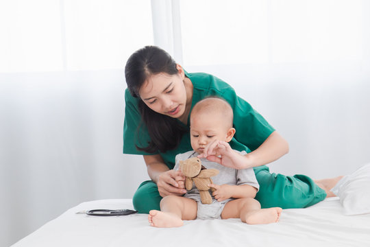 Asian toddler girl get sick examine by pediatrician doctor woman green uniform hold stethoscope, mother or beautiful nurse playing with adorable infant on floor bedroom, child health care concept
