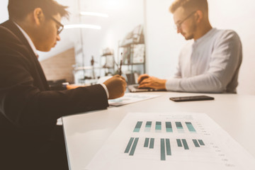 Young office worker sitting at desk, using computer. Two business man talking