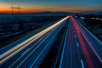 Fototapeta na wymiar Cars light trails on a straight highway at sunset. Night traffic trails, Motion blur, Night city road with traffic headlight motion.