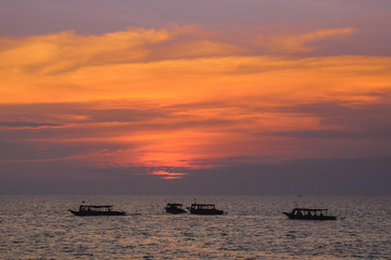 Group of boats on a wide sea during beautiful pink sunset in Cambodia Asia