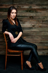 The concept of a glamorous portrait. Portrait of a pretty brunette girl in a black fashion suit on a stylish background in the original interior. Sits on a chair in various poses.