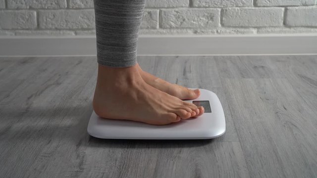 Woman staying on weighing scales, white brick wall background. Healthcare, diet concept. Close-up