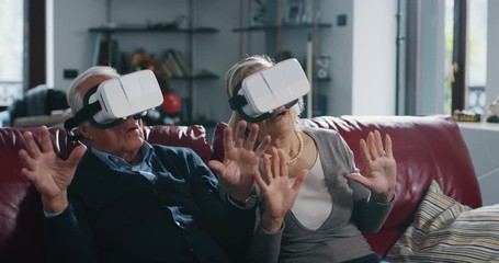 An excited senior couple is having fun using vr glasses in living room at home. - Powered by Adobe