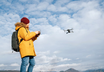 Teenager boy dressed yellow jacket piloting a modern digital drone using remote controller