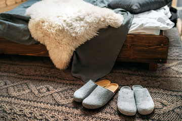 The two pair of gray home slippers near the wooden bed on the "knitted floor" in the cozy bedroom. Home sweet home concept image.