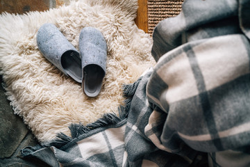 The pair of gray home slippers near the  bed on the white sheepskin in the cozy bedroom. Home sweet home concept top view image. - obrazy, fototapety, plakaty