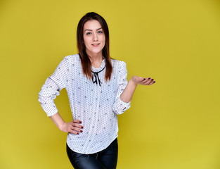 The concept of an office worker, teacher, manager. Portrait of a pretty brunette girl in a white business blouse smiling, talking to the camera on a yellow background.