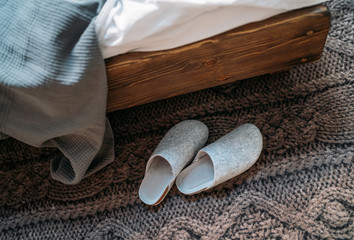 The pair of gray home slippers near the wooden bed on the 