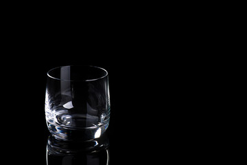 Empty glass for whiskey, brandy or bourbon on a black background with copy space.