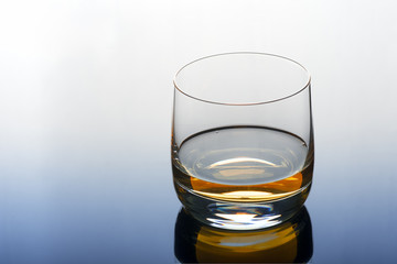 A glass of whiskey  on a transparent blue table.