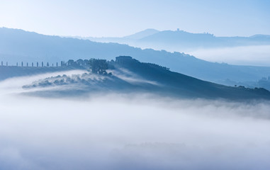 Morning fog in Tuscany. House on a hill with a vineyard and cypresses. Italy.