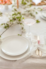 Table setting for a dinner with flowering cherry tree branches on the table. Vintage champagne glasses on the white linen tablecloth. Elegant name cards