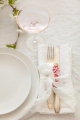 Elegant white table setting with silver cutlery, white plates and linen tablecloth. Wedding dinner decorations in white colour