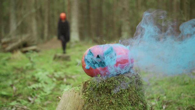 Person goes in mask and coak in the forest on the halloween with smoky pumpkin