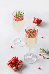 Pomegranate Christmas cocktail with rosemary, sparkling wine on white table. Xmas Holiday drink.