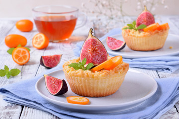 Grated mini pie with cottage cheese topped with pieces of figs and kumquats on ceramic plate