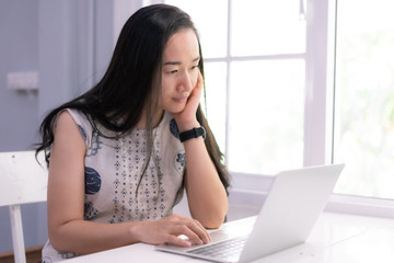 Beautiful asian girl using a notebook or laptop computer at her home and smiling happily.