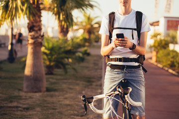 Young handsome guy equipped cyclist smiles and chats with his girlfriend using a smartphone on a sunny summer day while relaxing from a trip. Vacation activities concept