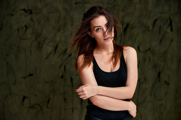 Fototapeta premium Beauty concept, stylish portrait. Photo of a pretty glamorous brunette girl in a black t-shirt with flying hair on a gray fashionable original background.